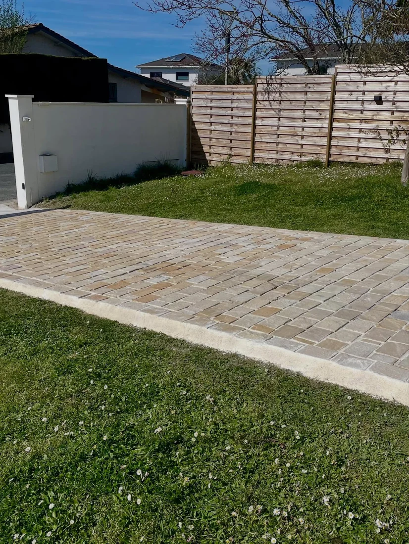Allée pavée terminée par SH Terrassement dans un jardin, entre pelouse et clôture